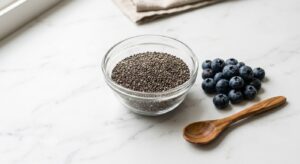 A professional, high-angle editorial photograph of a glass bowl filled with chia seeds next to fresh